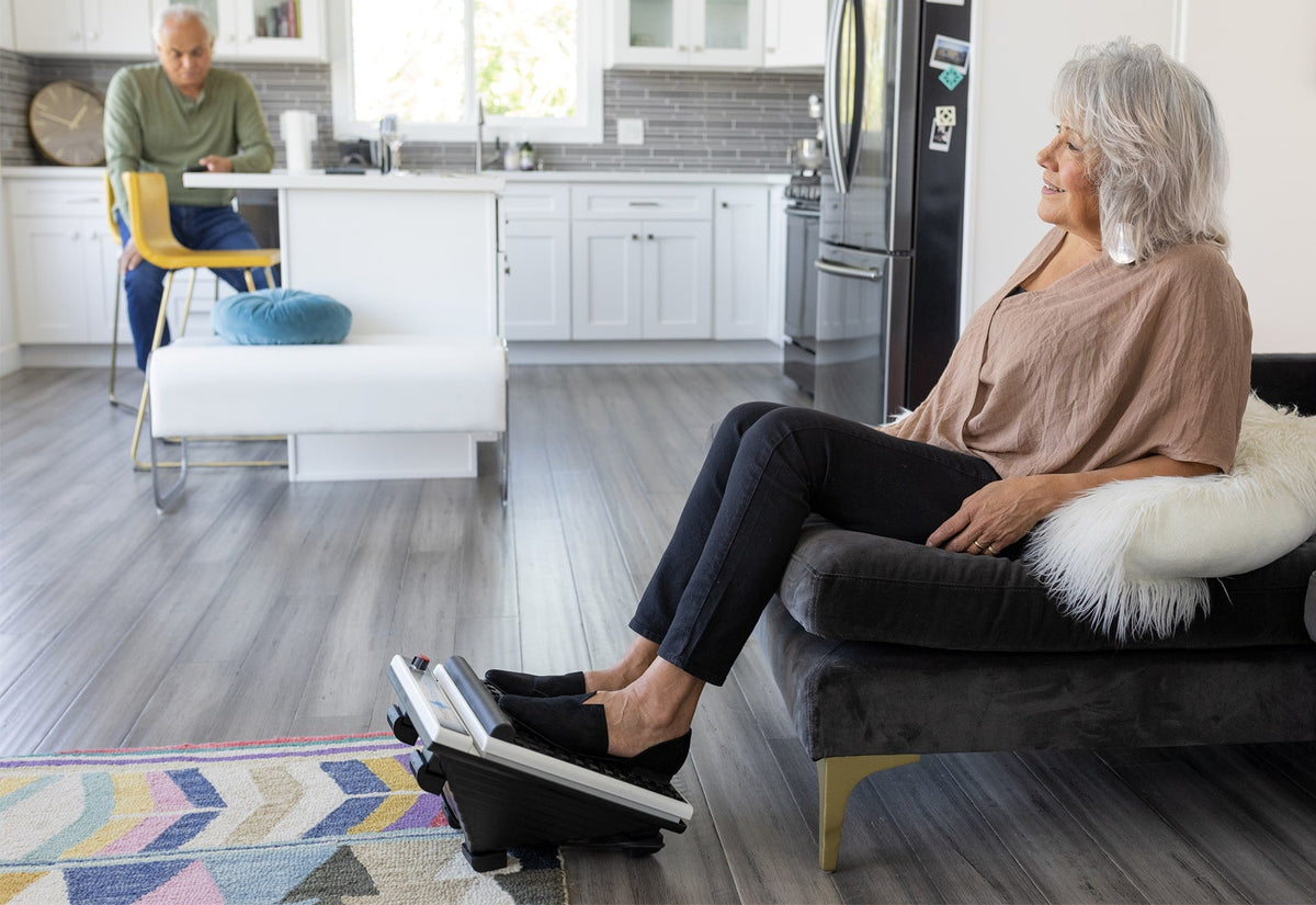 Woman relaxing on a sofa at home with her feet on a MedMassager Foot Massager Plus.