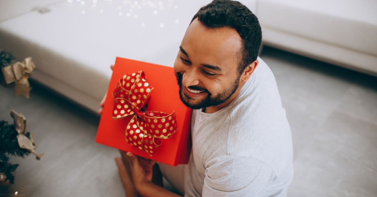 Joyful man with beard holding a red gift with festive bow indoors, celebrating Christmas.