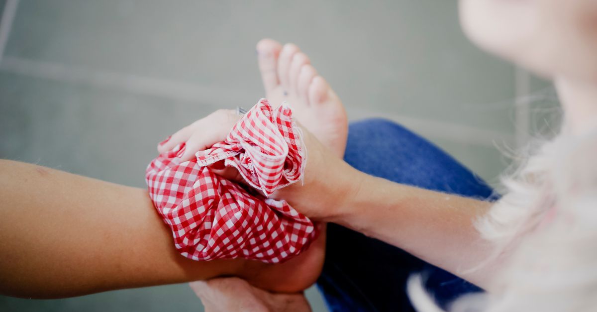 Close-up of a person using a checkered ice pack on an injured ankle, promoting injury care and relief.