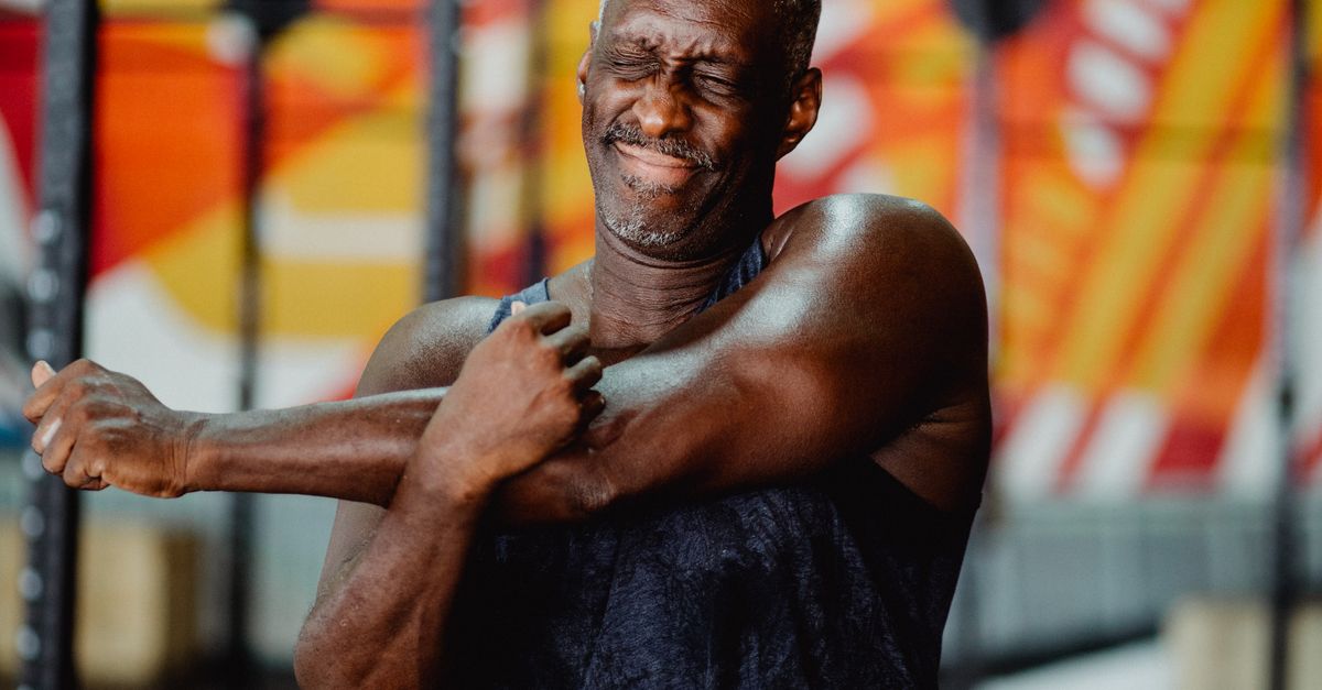 Older man stretching one arm across his body indoors.