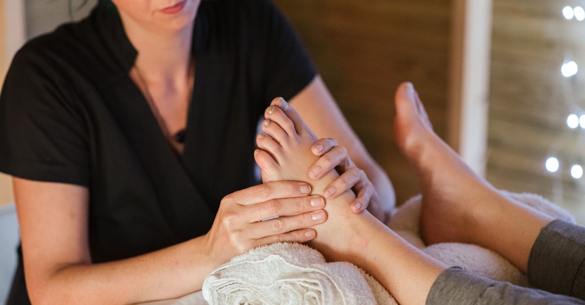 Unrecognizable barefoot female client lying with legs on towel in spa salon while receiving feet massage from therapist on blurred background