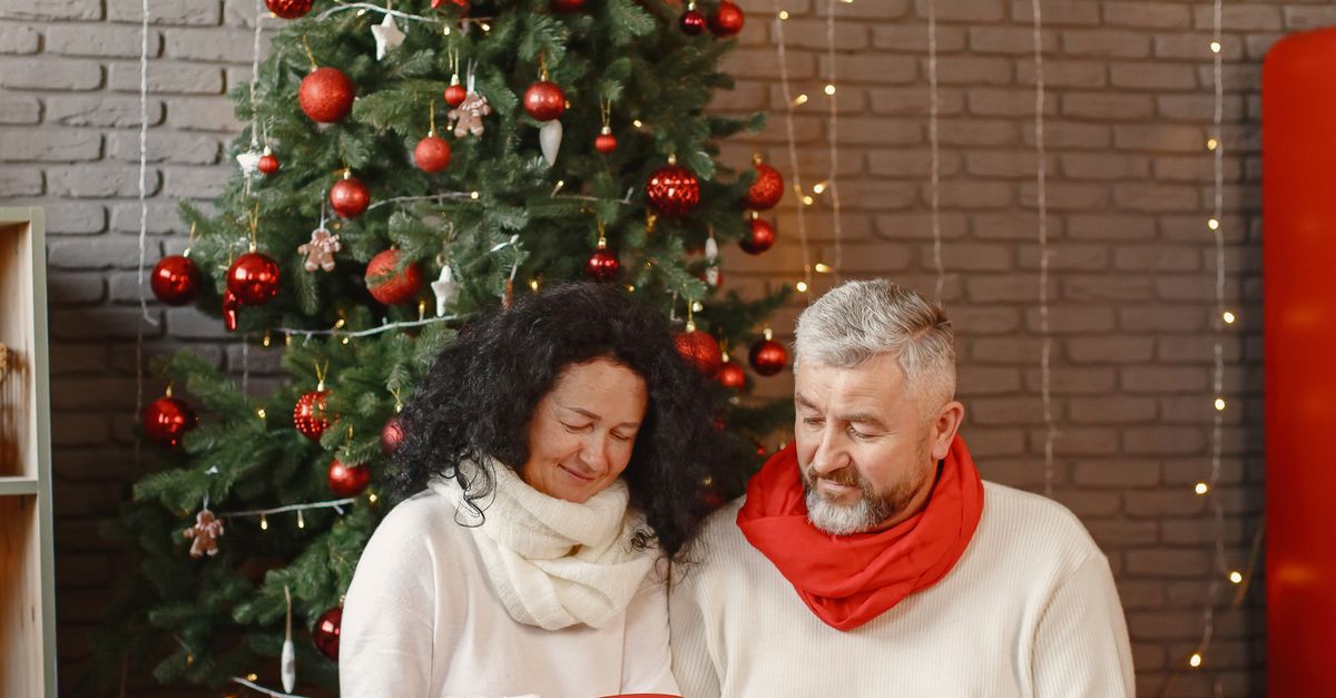 Older couple exchanging gifts by a Christmas tree.