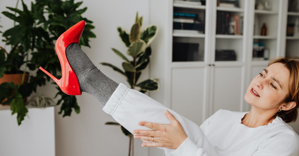 A woman indoors, trying on striking red high heels, showcasing a fashion-forward moment.