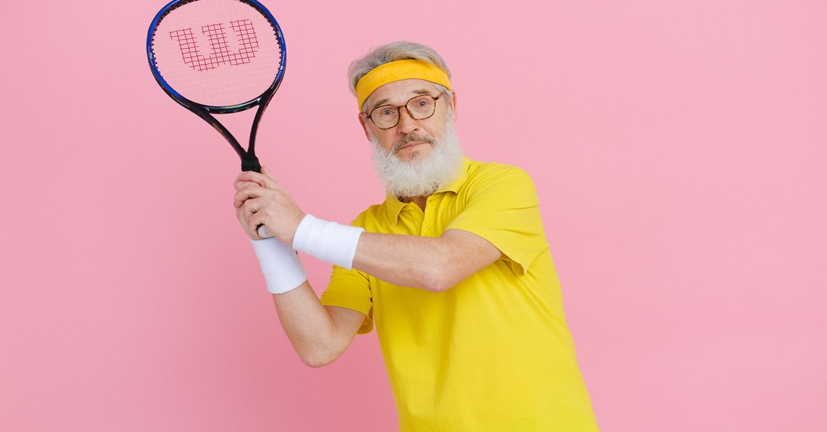 Elderly man in yellow sportswear holding a tennis racket against a vibrant pink background.