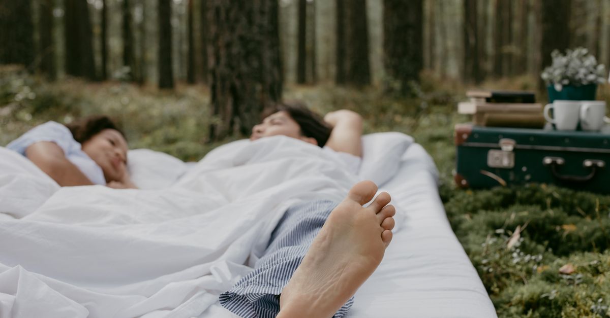 A couple peacefully resting on a white blanket in a forest setting, capturing tranquility and nature.