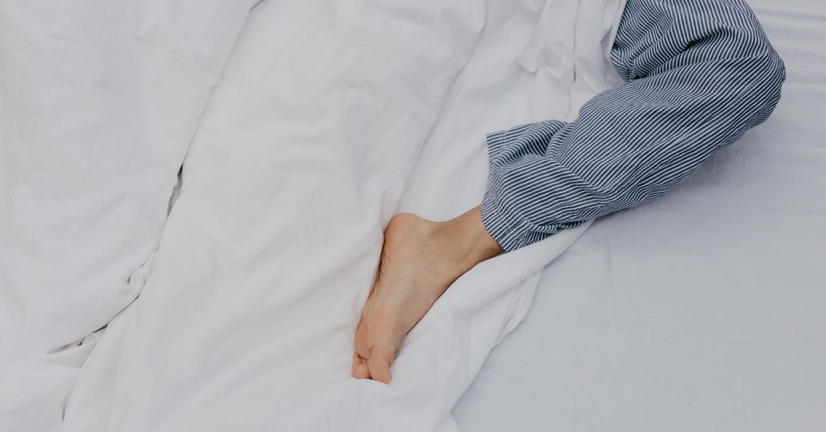 Relaxed morning with a foot peeking from under white bedding, wearing striped pajamas.