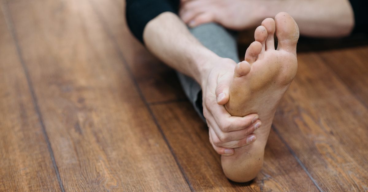 Close-up of a person doing a stretching exercise on a wooden floor, focusing on their bare foot.