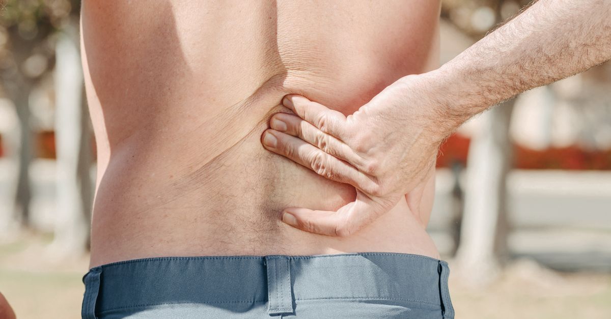 Close-up of a man holding his lower back in pain, possibly indicating discomfort or injury.