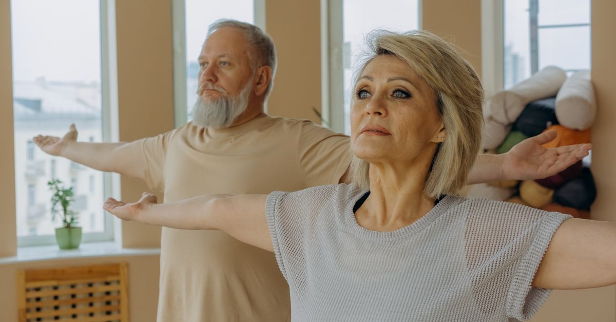 Older couple stretching their arms out wide in a bright room.