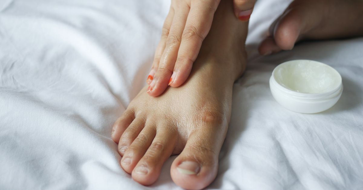 Close-up of a person applying moisturizer to their foot, promoting skin care and hygiene.