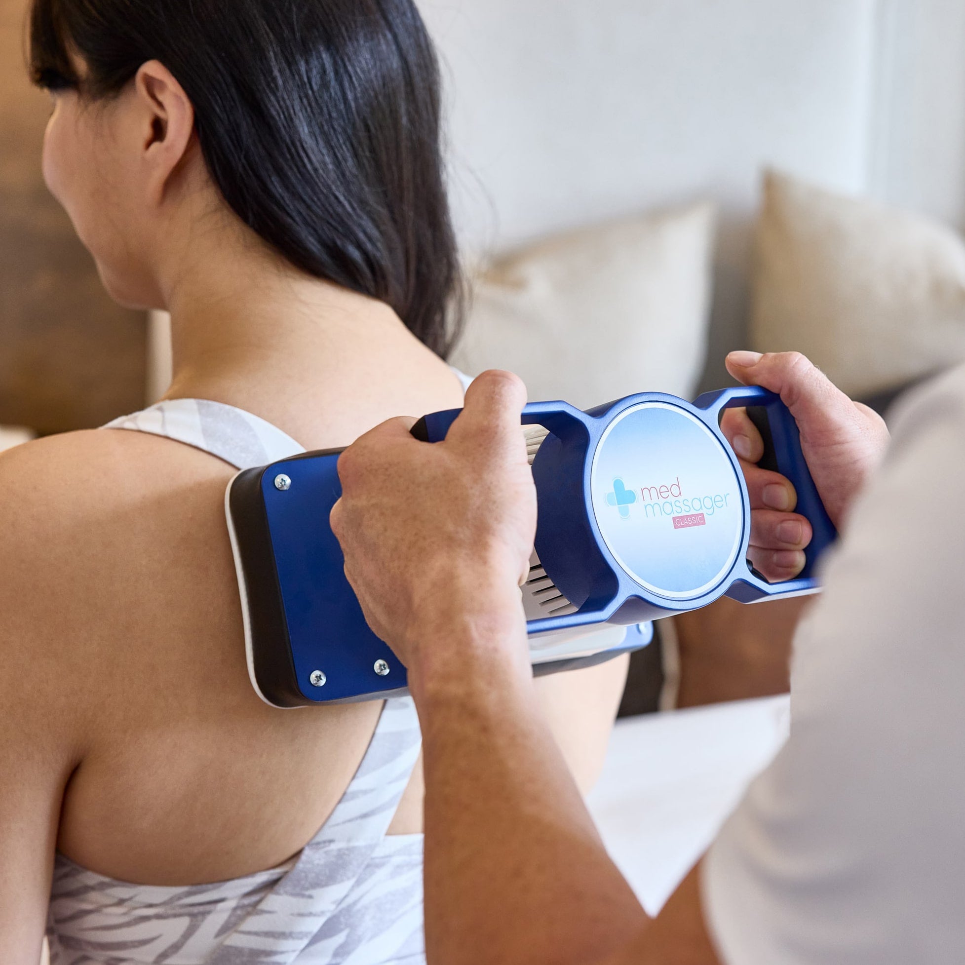 Close-up of a person using the MedMassager Classic body massager on a woman’s shoulder