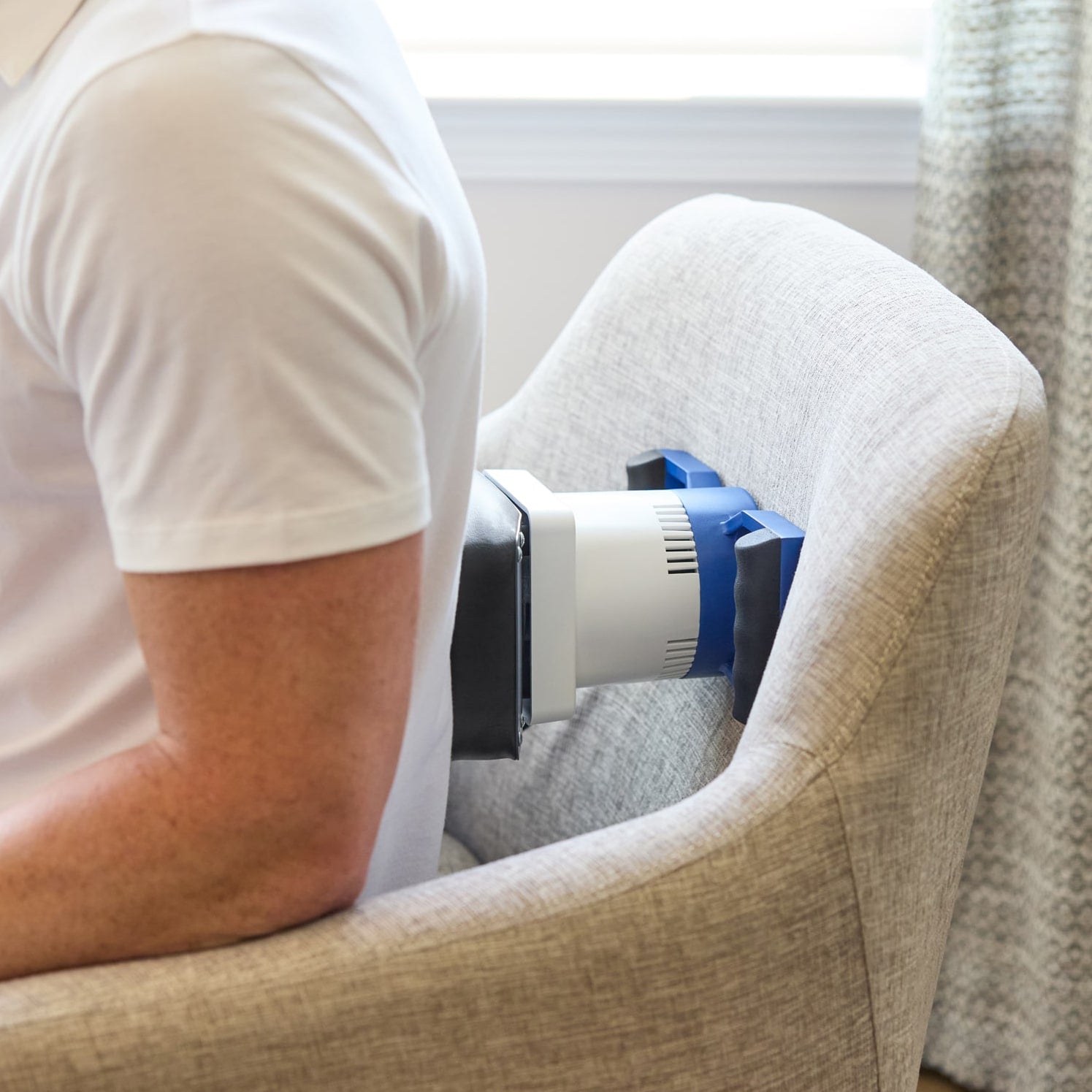 Back view of a person using a body massager classic between their back and the backrest of a chair