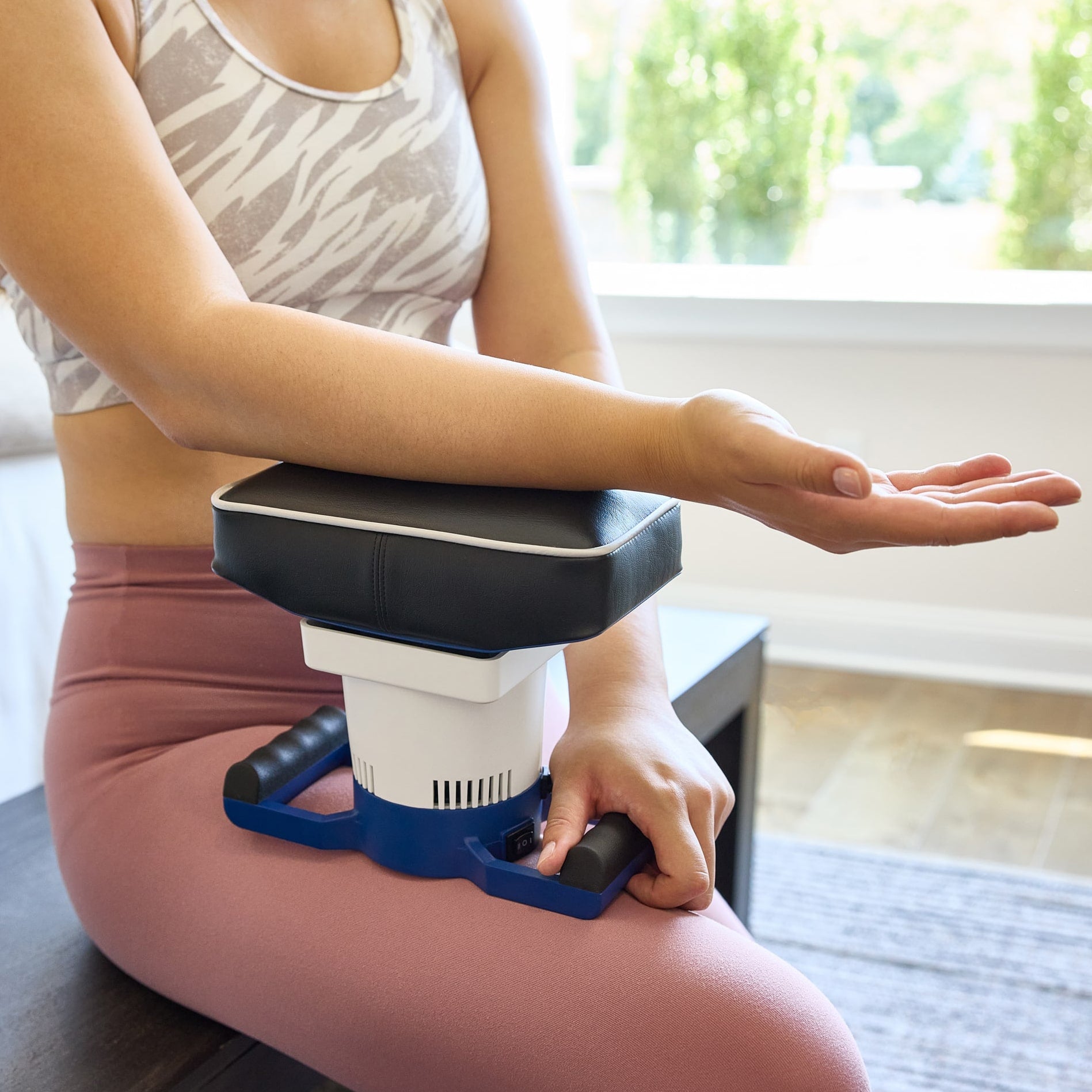 Person using a body massager classic on their forearm while seated on a bench