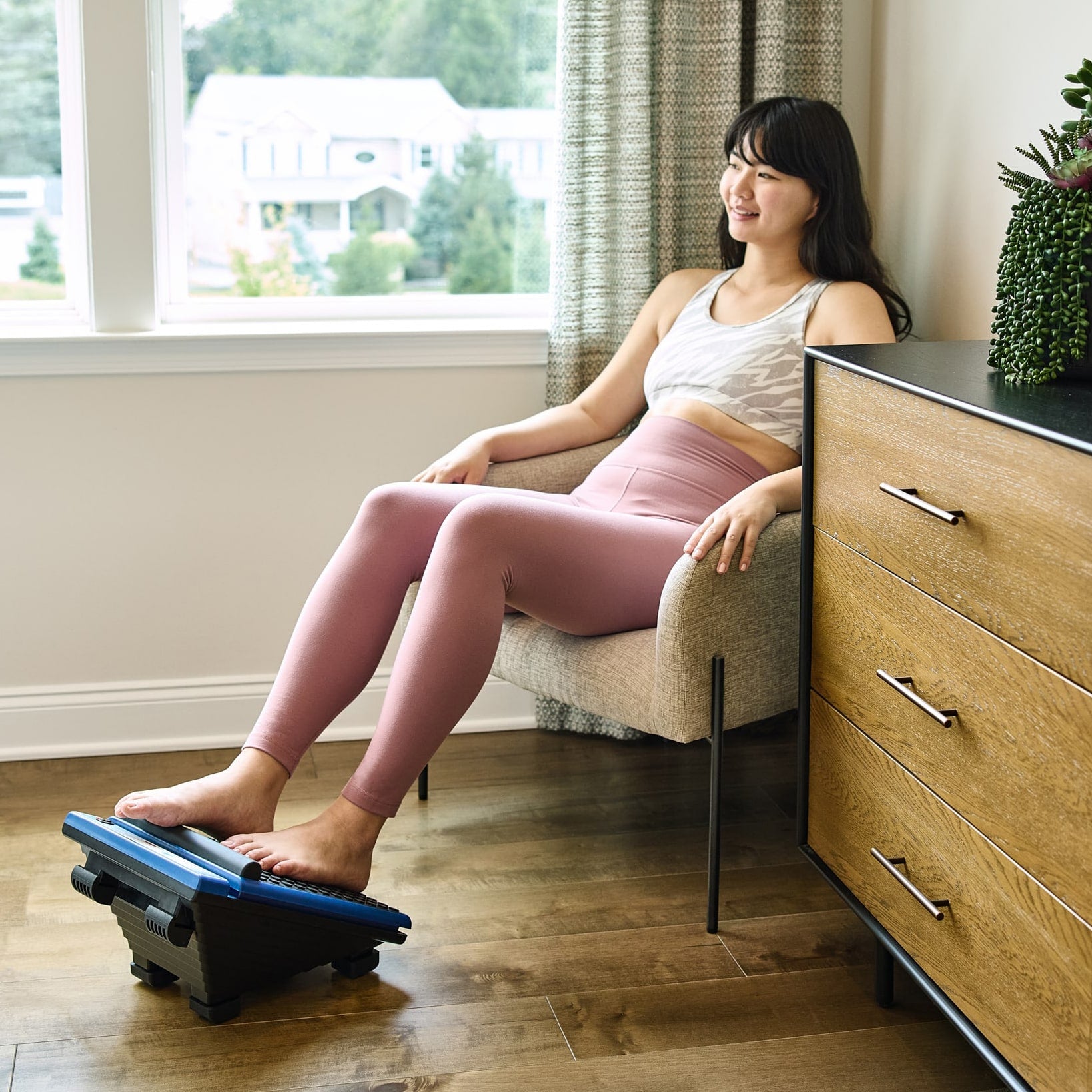 Woman using the MedMassager Classic foot massager while seated by a window in a home setting