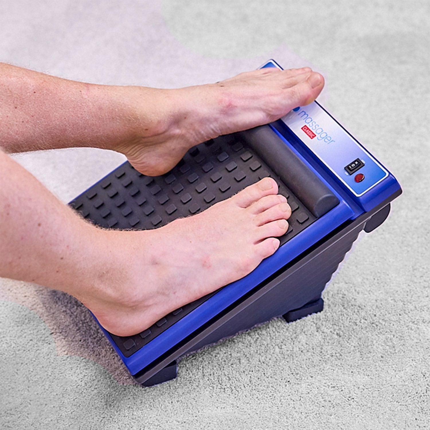 Man using the MedMassager Classic foot massager while seated on a carpeted floor