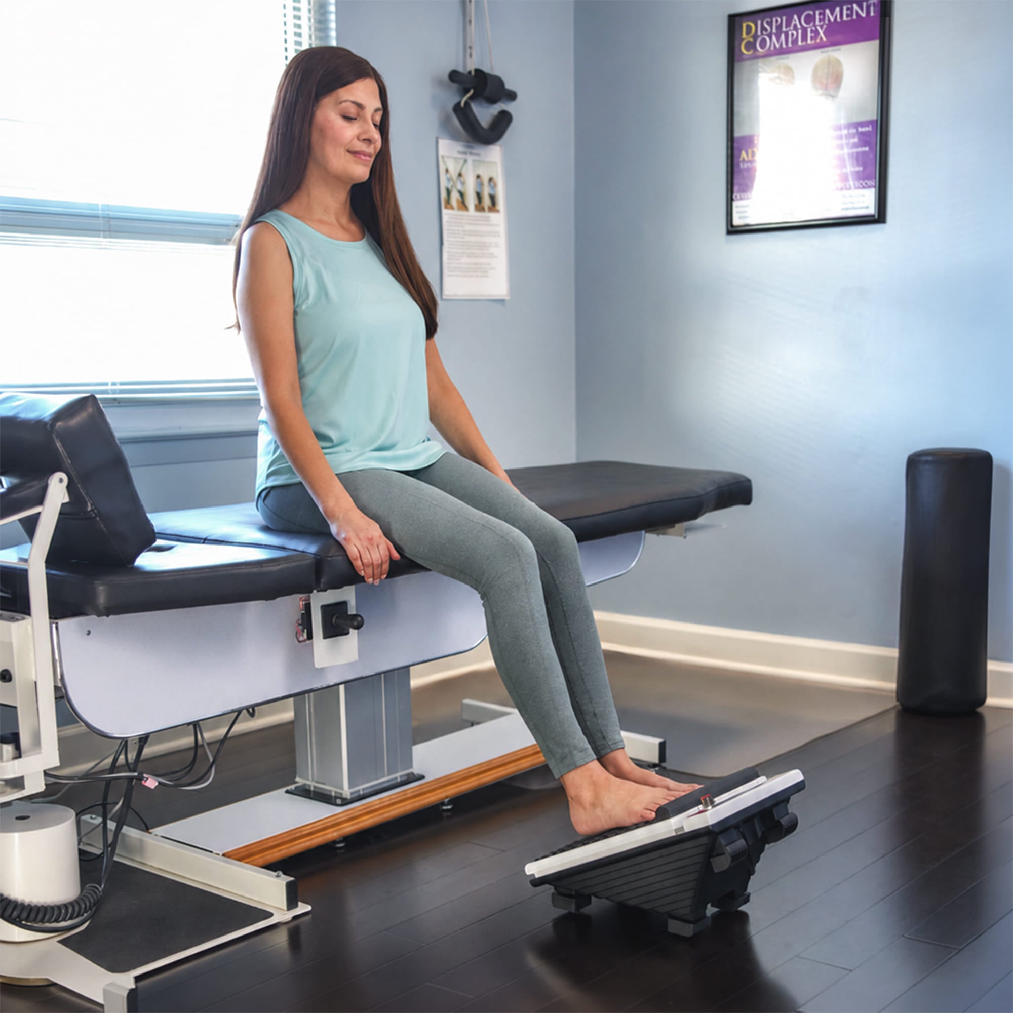 Woman using a MedMassager foot massager on exam table for nerve pain relief.