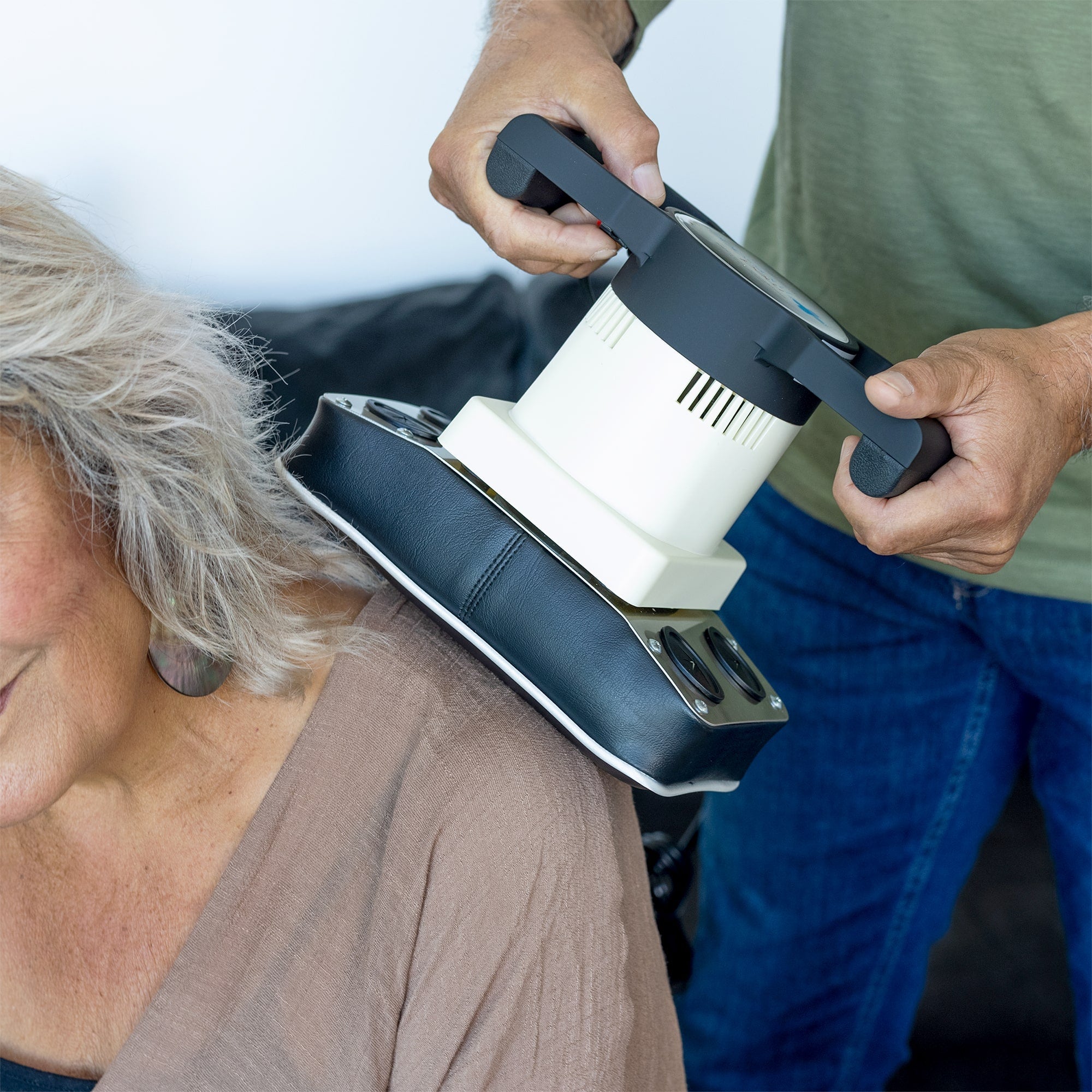 Body massager being used on a woman's upper back and shoulder in a home setting.