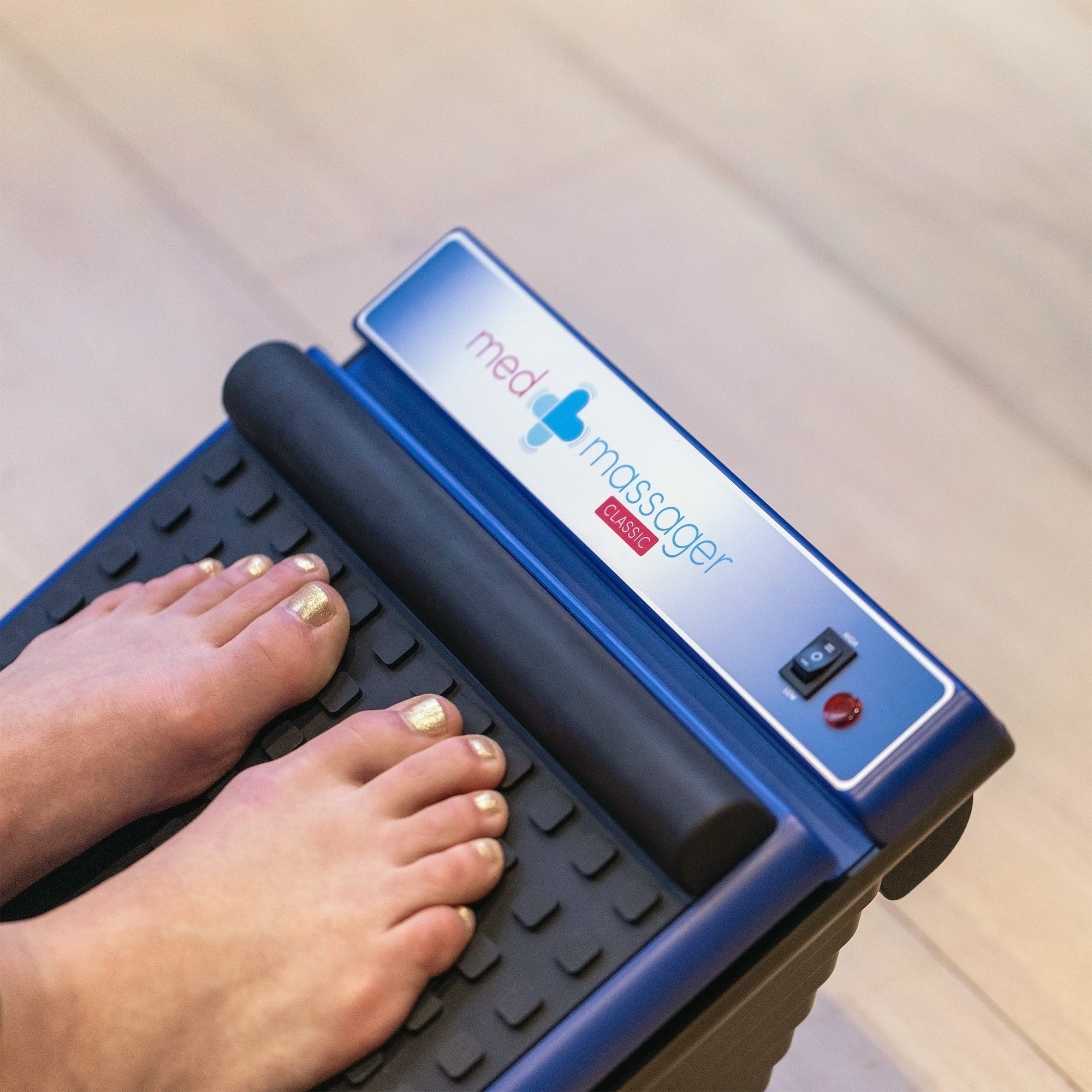 Close-up of toes resting on the MedMassager Classic foot massager with the logo and power switch visible