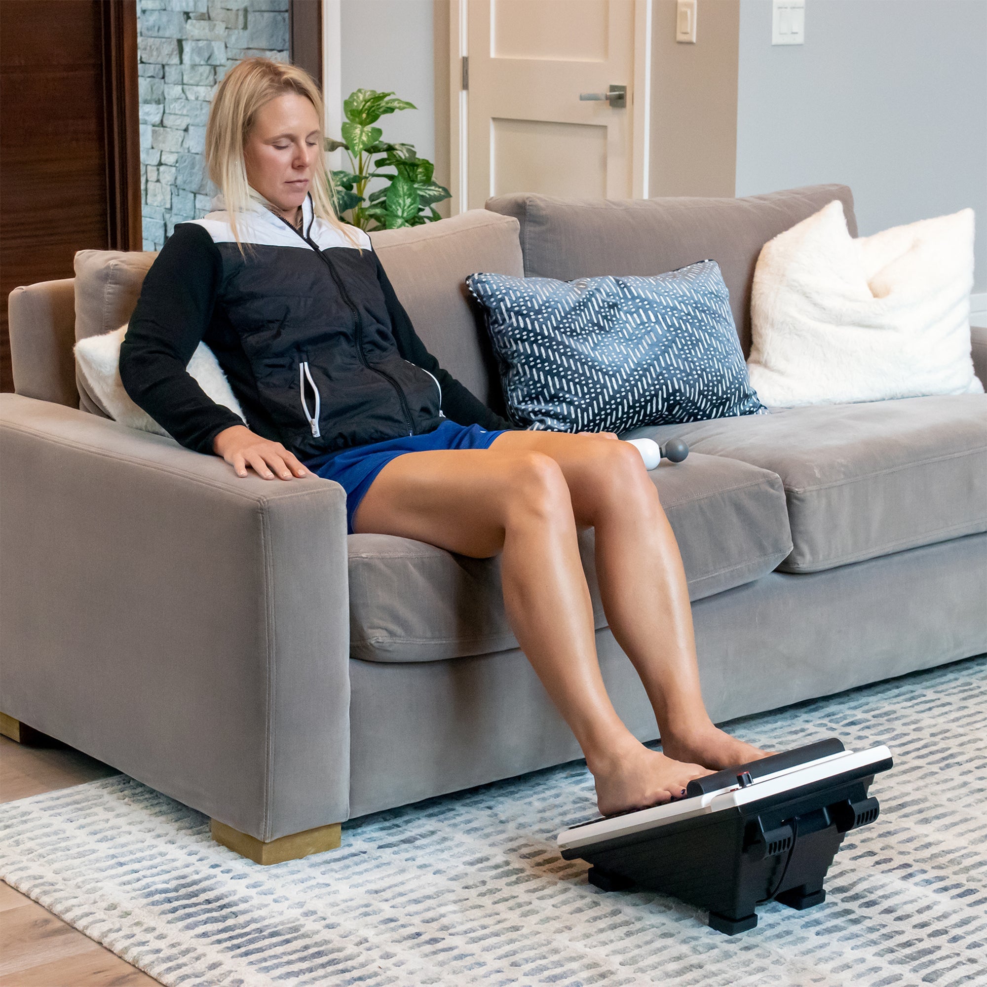 Person relaxing on couch while using the Foot Massager Plus on bare feet