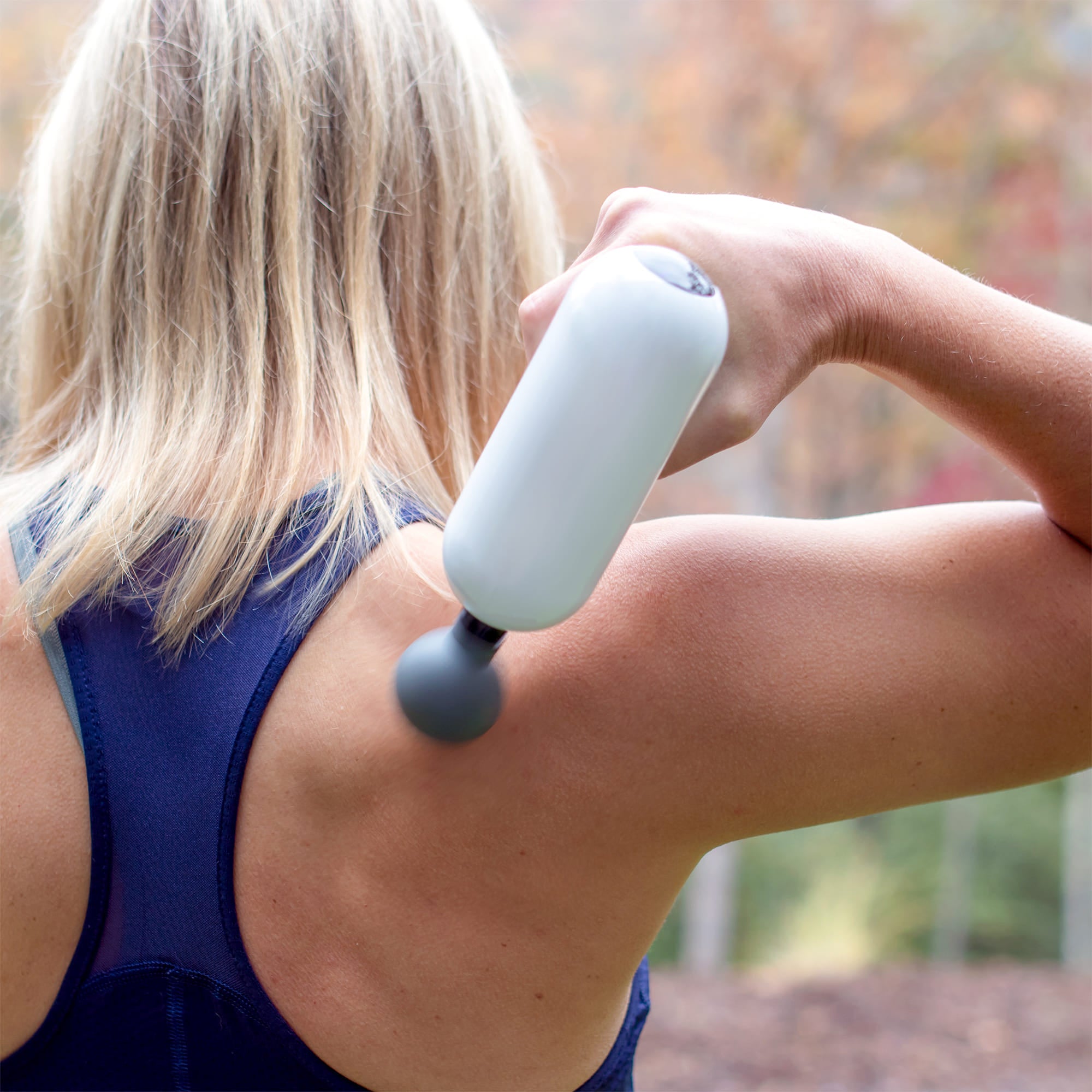 Woman using Accuvibe Mini massager on shoulder outdoors