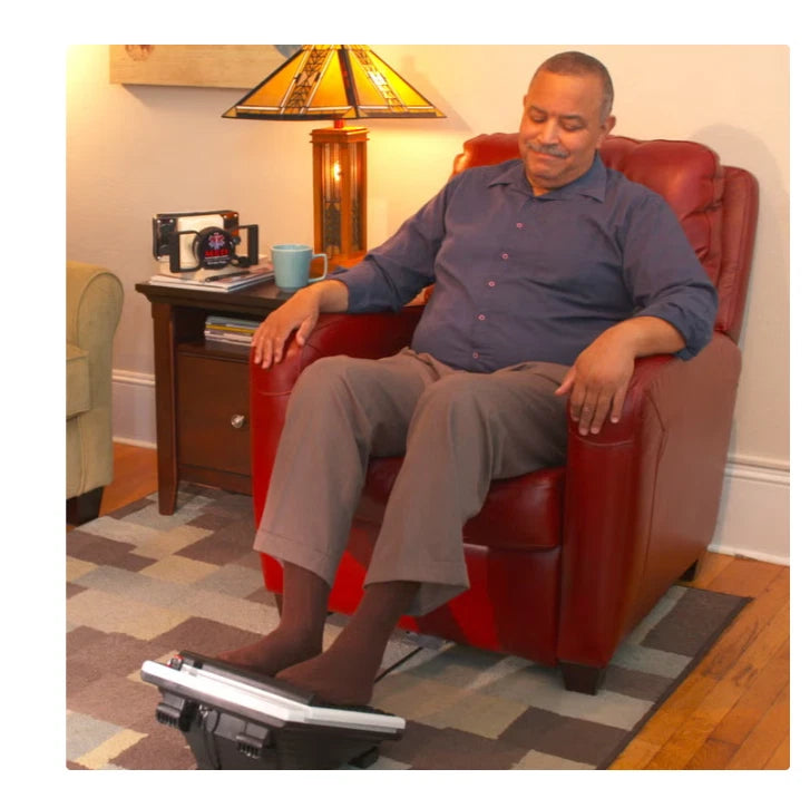 Man sitting in a red armchair with his feet resting on a MedMassager foot massager.