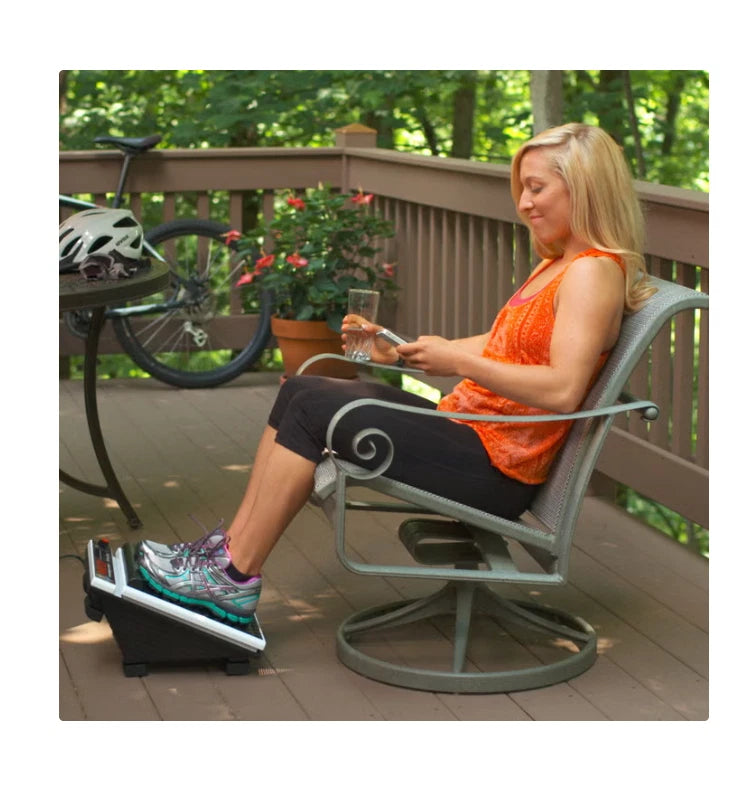 A woman on a deck uses a MedMassager foot massager while looking at her phone.
