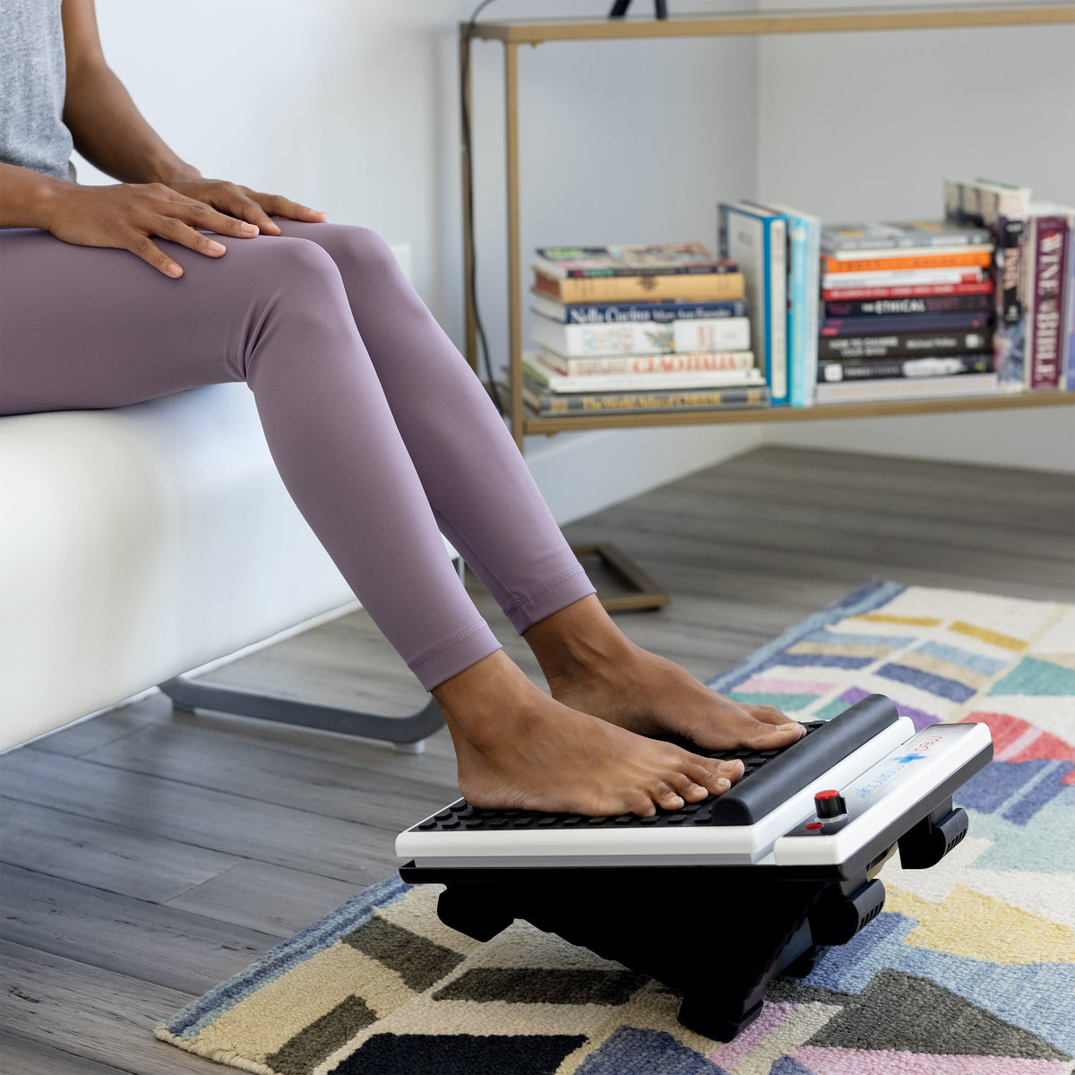 Bare feet resting on a MedMassager Foot Massager in a modern living room.