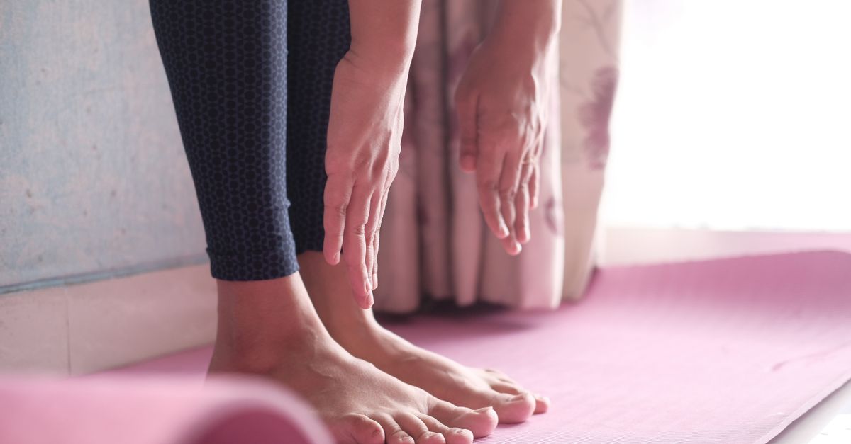 Close-up of a person doing a yoga pose on a pink mat indoors, showing feet and hands.