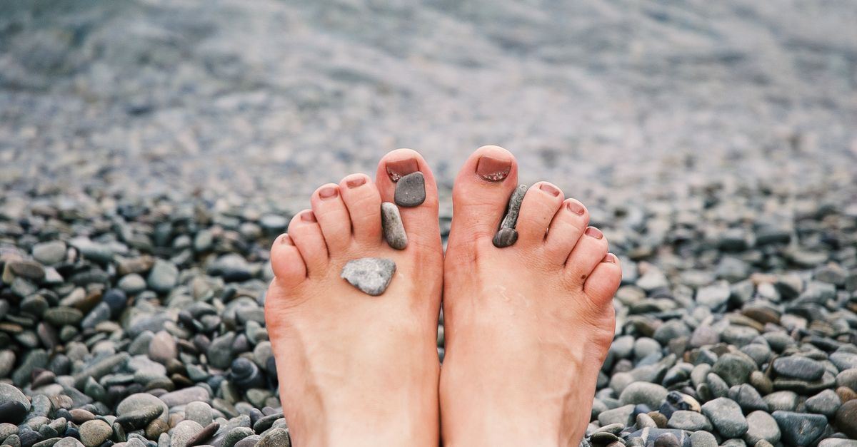 Close-up of female feet with stones on pebbled beach by the water, evoking relaxation and tranquility.