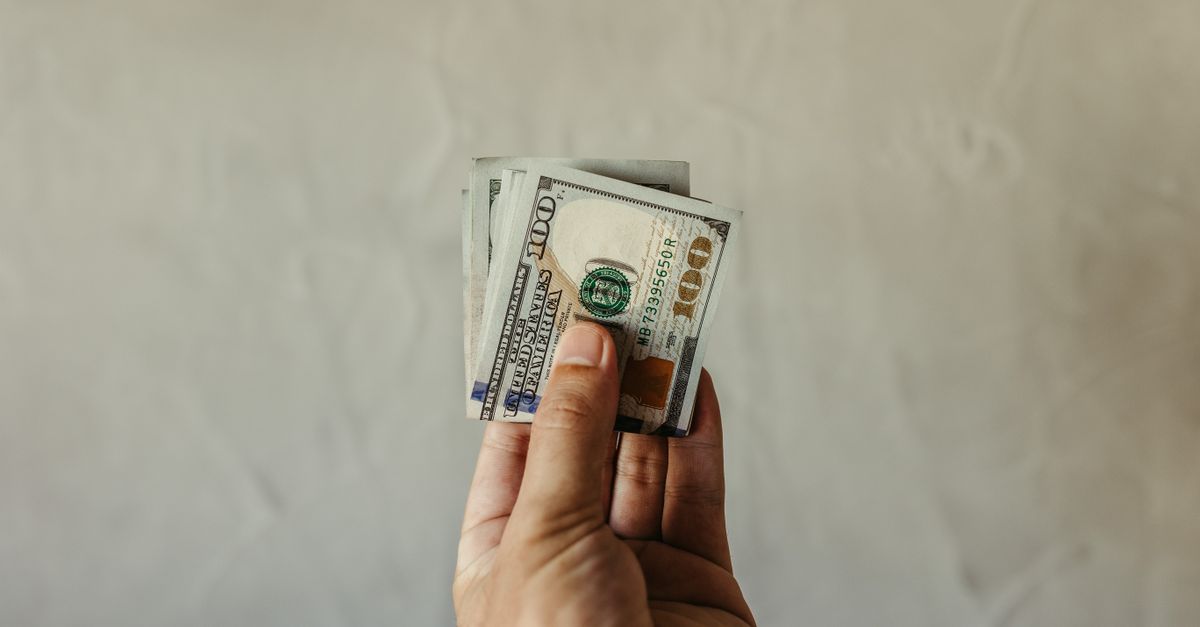 A clear view of a human hand holding a stack of US dollar bills, symbolizing finances.