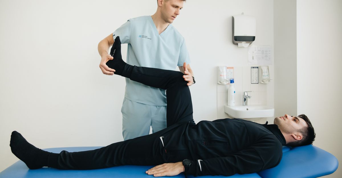 A physiotherapist assists a patient with leg stretching exercises on a treatment table.