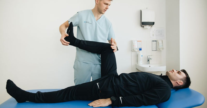 A physiotherapist assists a patient with leg stretching exercises on a treatment table.