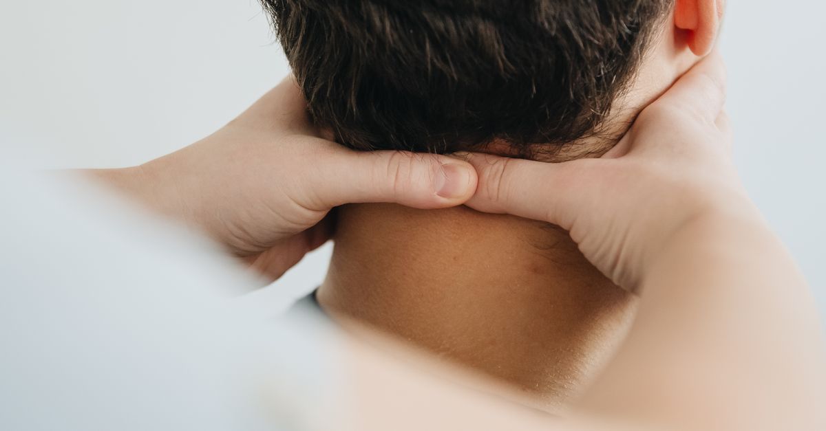 Close-up of a person touching the back of their neck at the base of the skull.