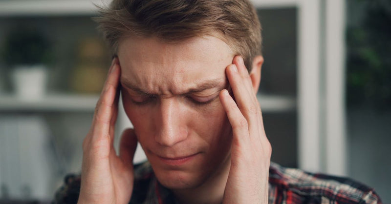 Man experiencing stress or headache, closing eyes and rubbing temples indoors.