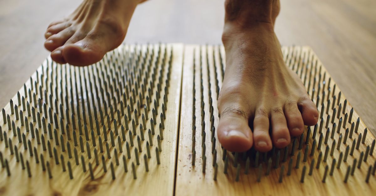 Bare feet on a wooden board with nails for a unique wellness experience.