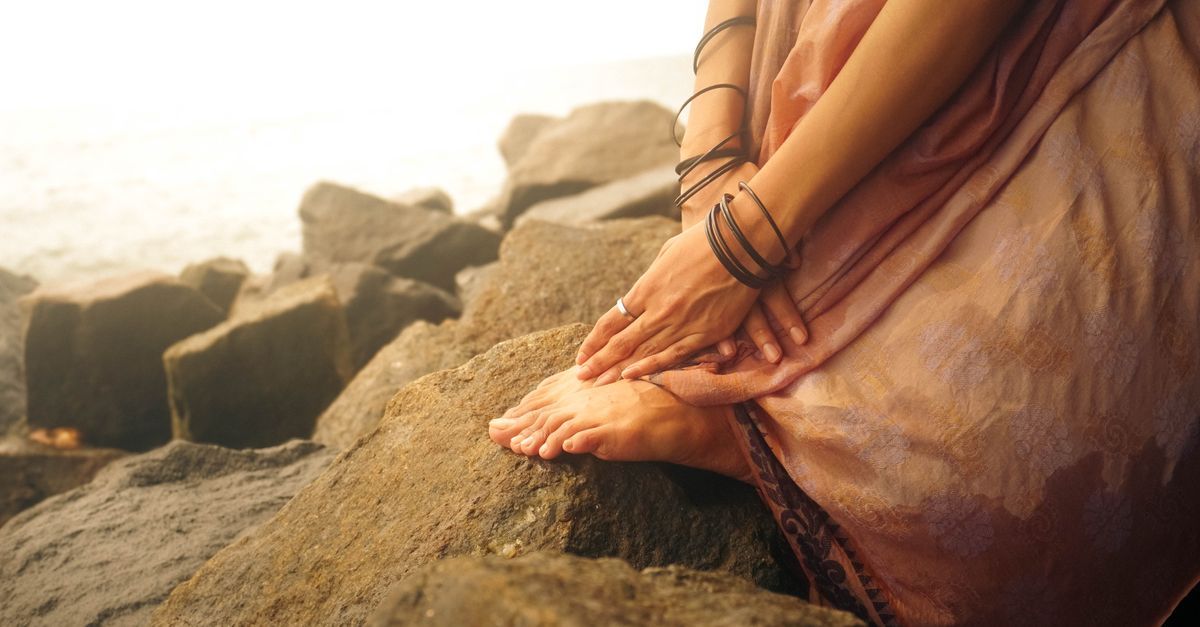 Tranquil scene of a woman sitting on rocks by the sea, enveloped in warm tones of sunrise.