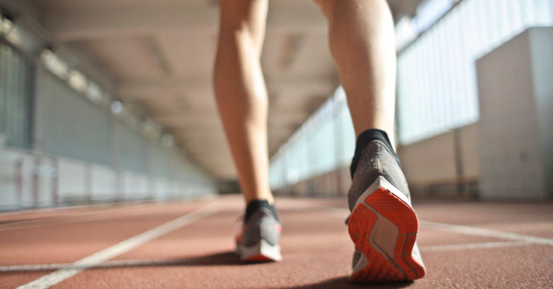 From below back view of crop athlete in sports shoes standing on running track while preparing for start during training