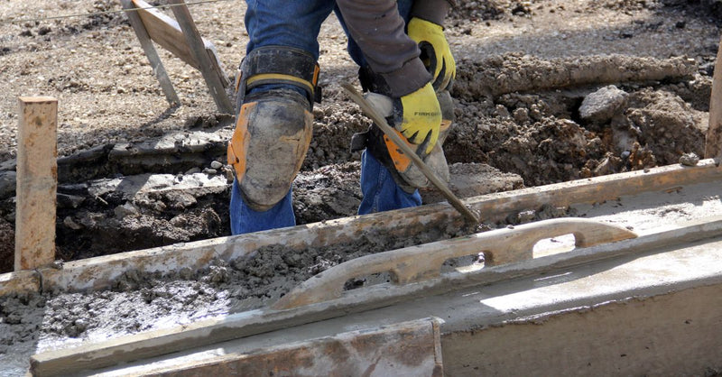 Worker using a trowel to smooth concrete at an outdoor construction site.