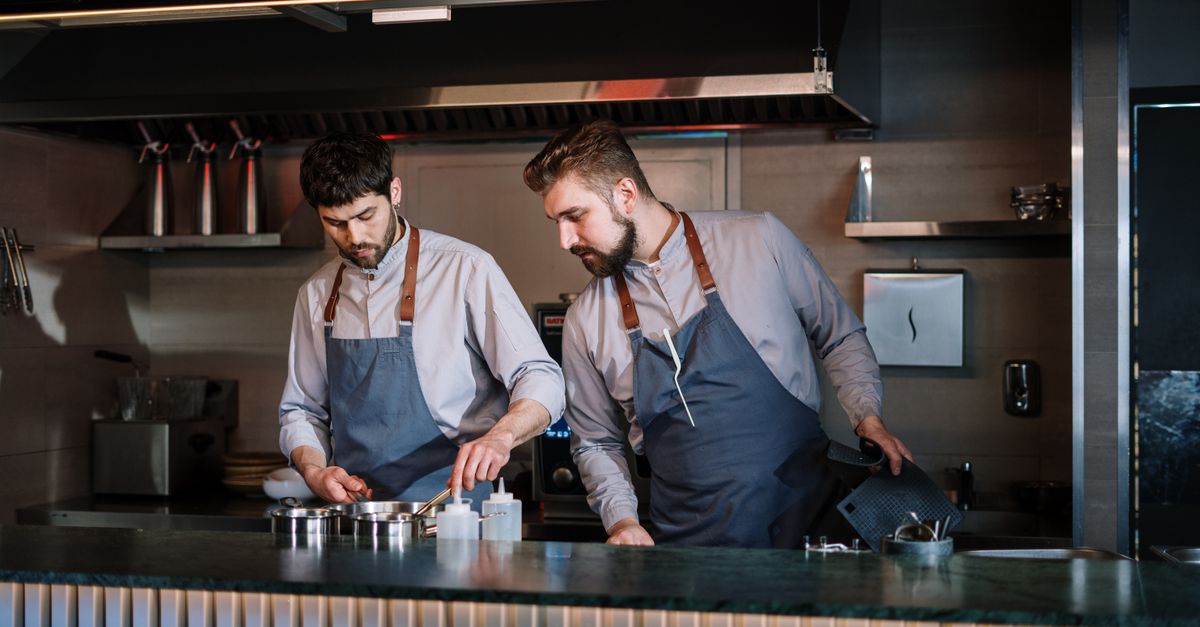 Two chefs in aprons cooking in an open restaurant kitchen.