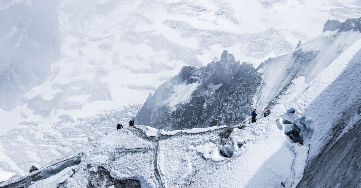 From above distant brave alpinists in winter clothes climbing on rough stiff mountain slope covered with ice and snow on high altitude