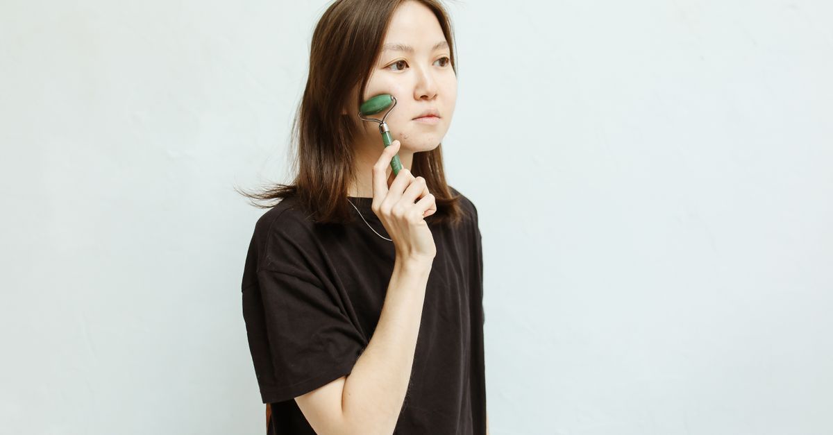 Asian woman using jade roller for facial massage and beauty routine indoors.
