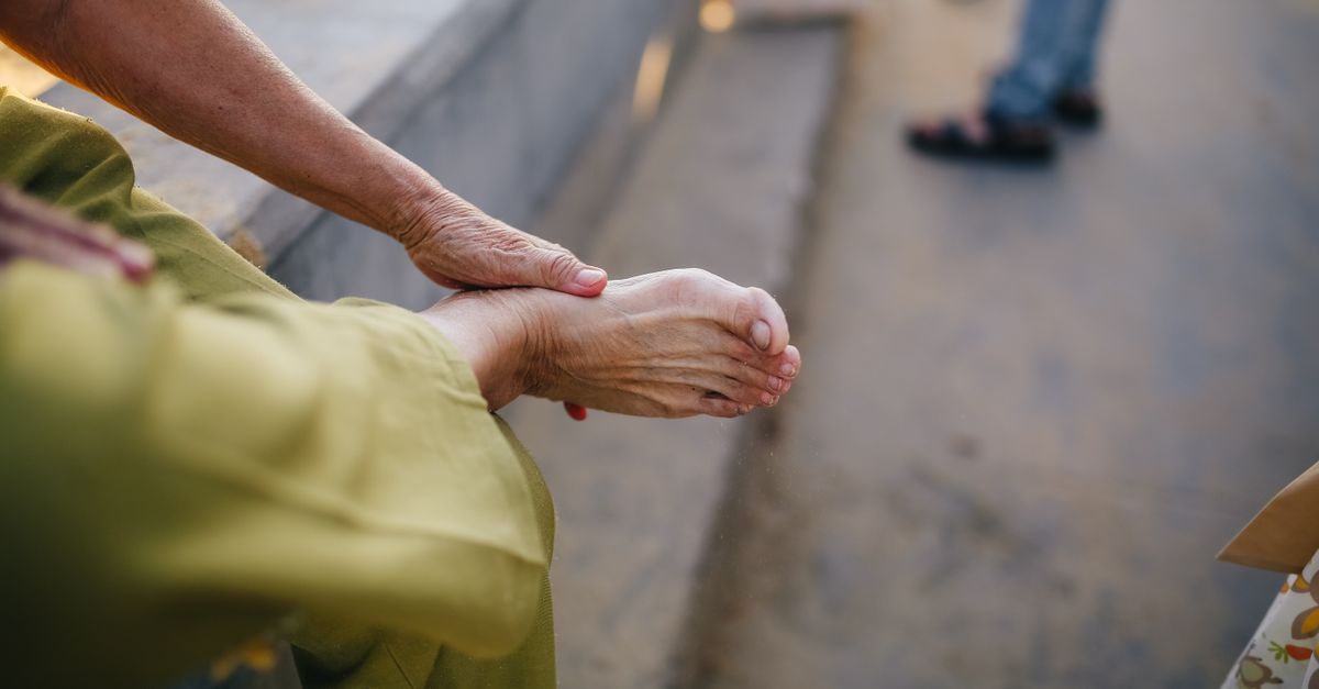 An elderly person sitting outdoors massaging their foot for relief.
