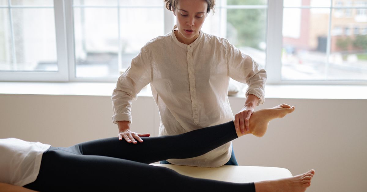 A therapist provides leg massage therapy to a client in a serene clinic setting.