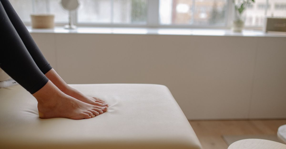 A woman's feet in leggings resting barefoot on a light colored cushioned surface indoors.