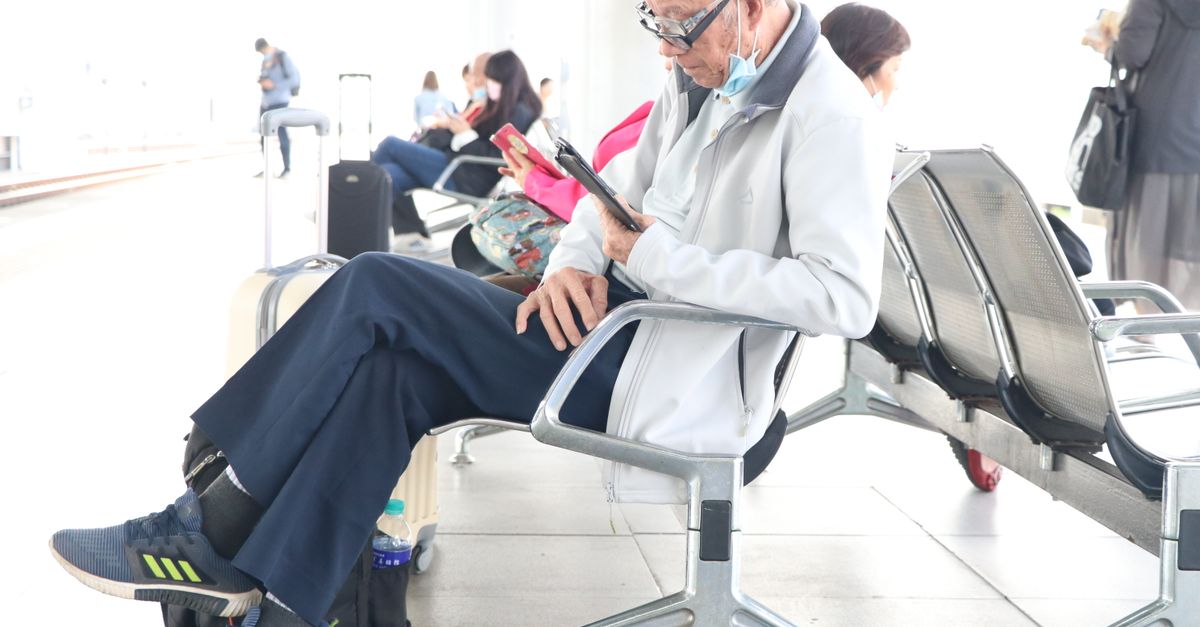 Older traveler sitting in an airport terminal with luggage nearby.