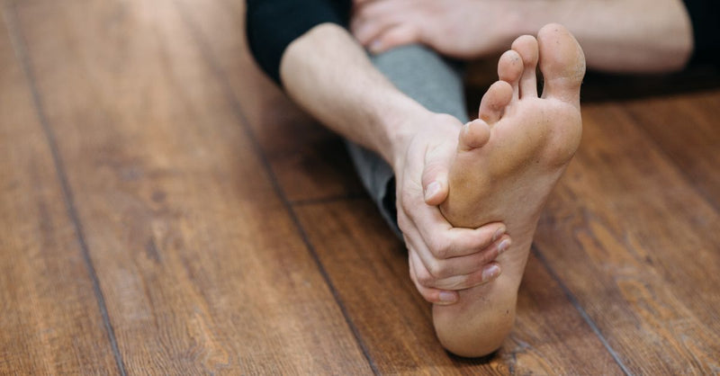 Close-up of a person doing a stretching exercise on a wooden floor, focusing on their bare foot.