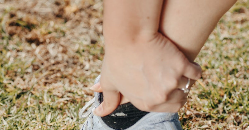 Person in sneakers holding their lower calf and ankle.