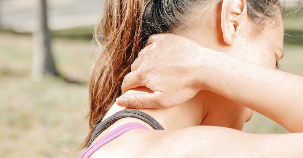 A woman massages her neck outdoors, relieving discomfort and tension.