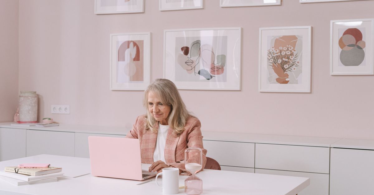 Older woman working on a laptop at an office desk.
