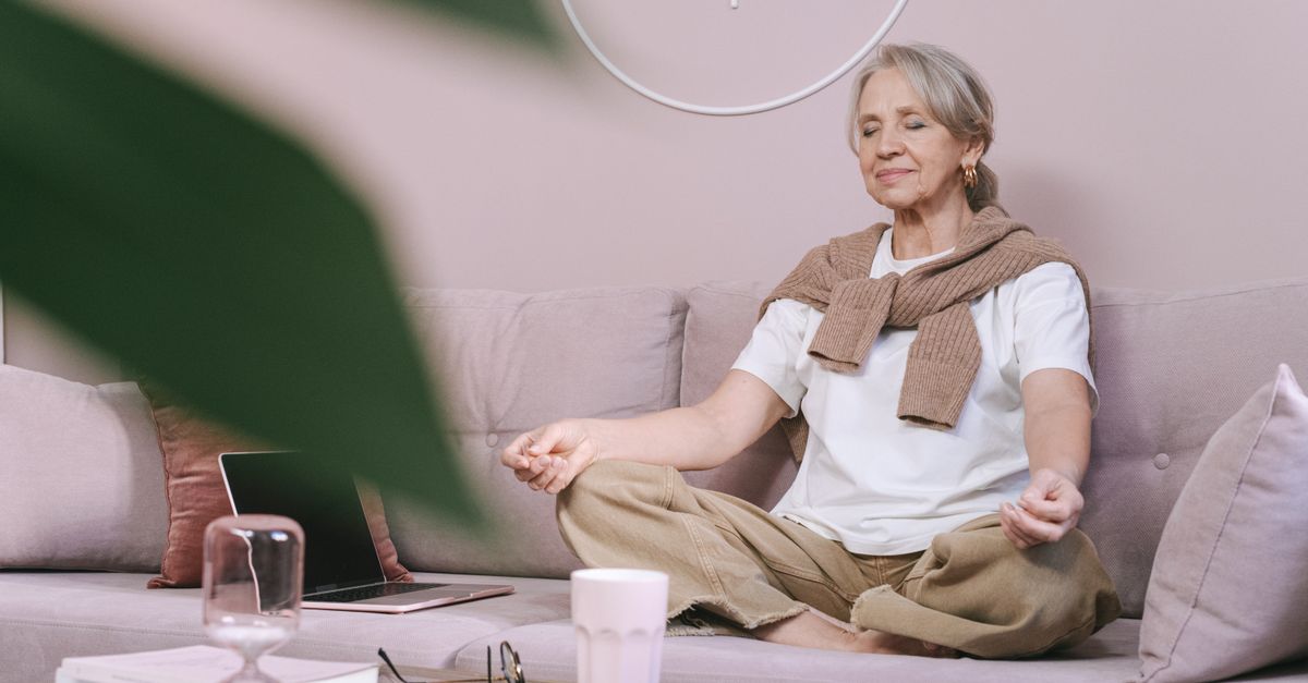 Elderly woman sitting on a sofa with eyes closed, in a peaceful home setting.